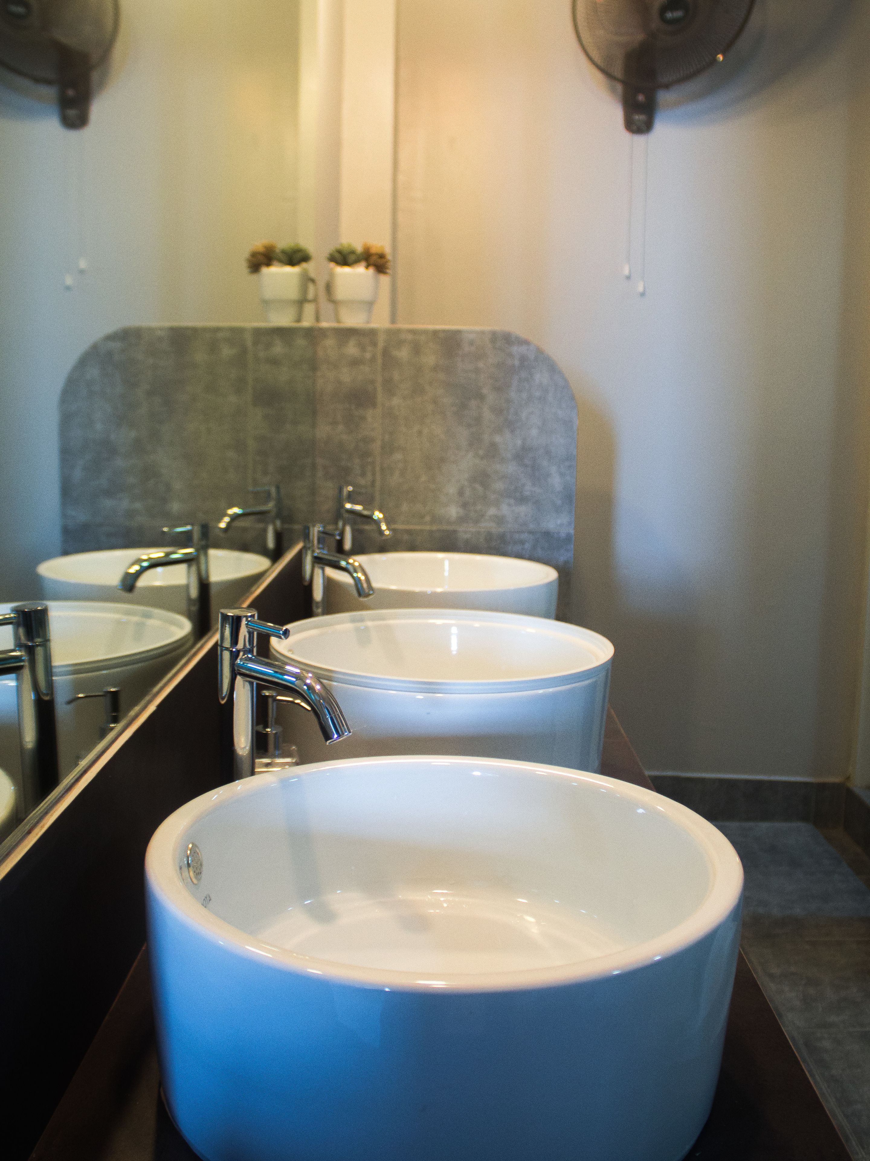 Une salle de bain avec trois lavabos, un miroir et un ventilateur.