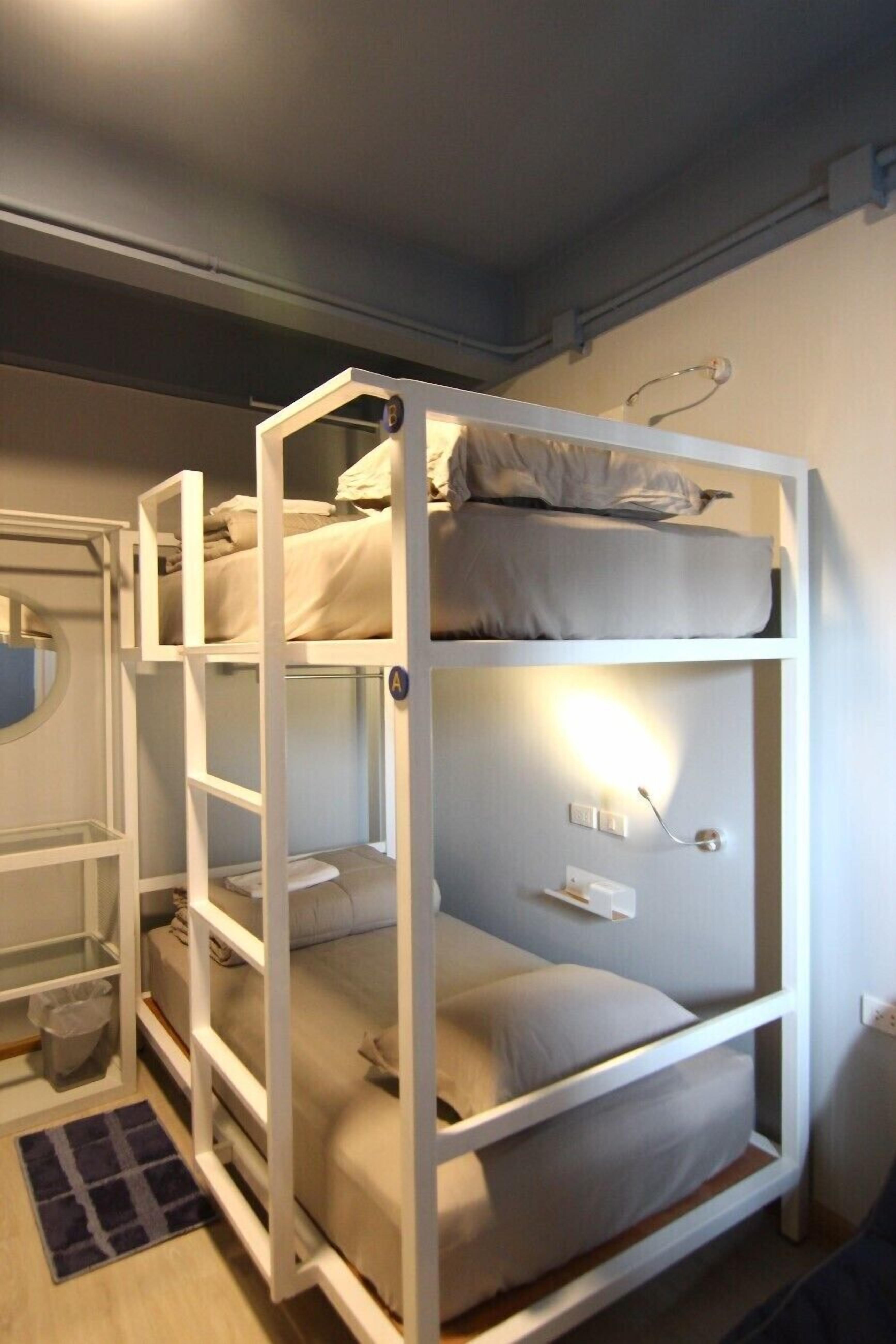A bunk bed with three levels, a small shelf unit, and a circular mirror.
