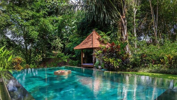 A clear, rectangular swimming pool with a tiled deck, surrounded by lush greenery and a small gazebo. - Sari Bamboo Villas (Ubud)