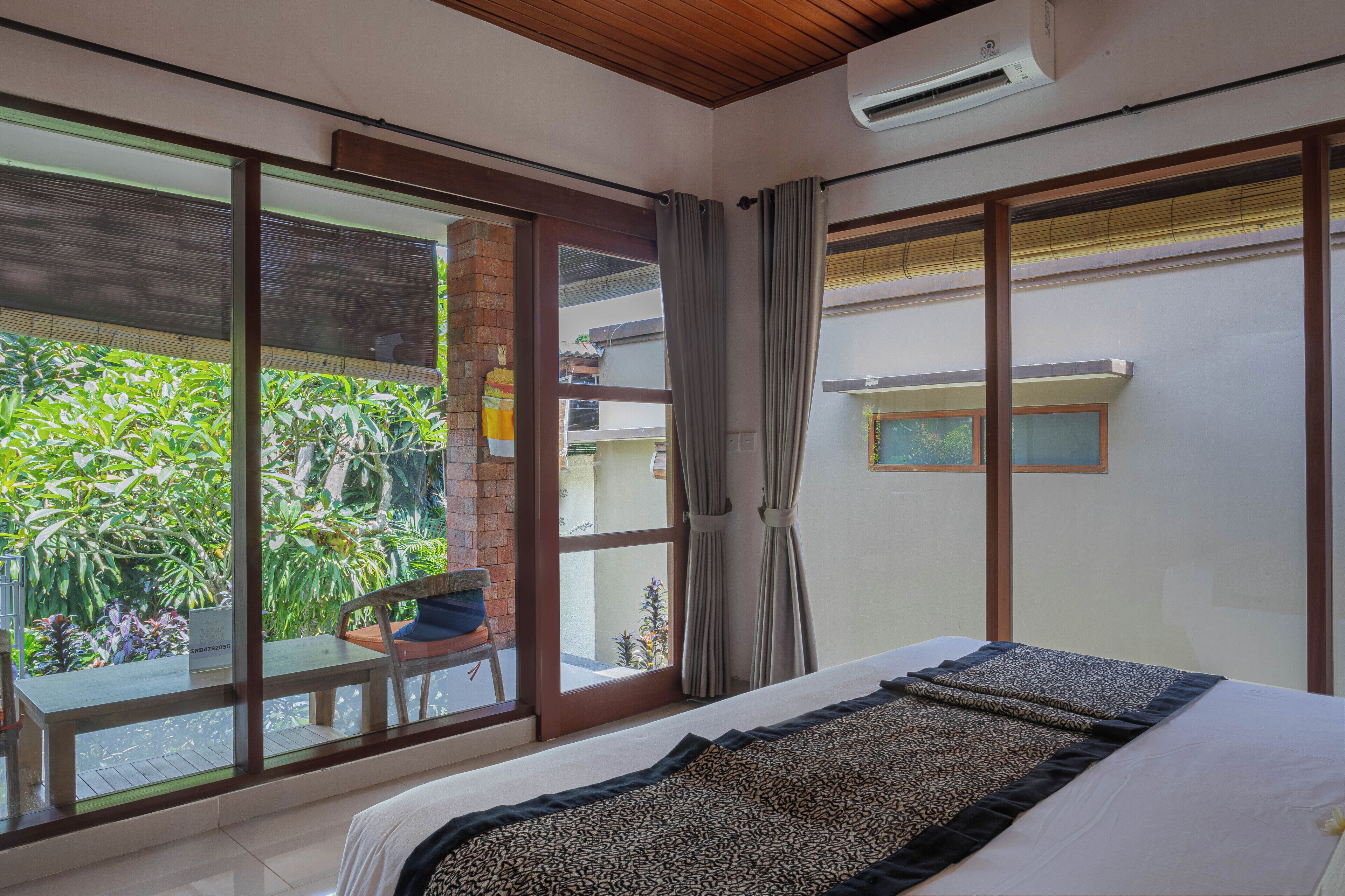 A bedroom with a large window, a bed, a chair, and a small table.