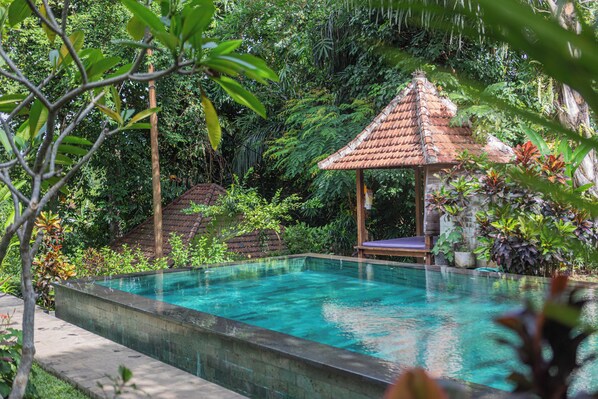 A rectangular swimming pool with a tiled roof structure in the background, surrounded by lush greenery. - Sari Bamboo Villas (Ubud)