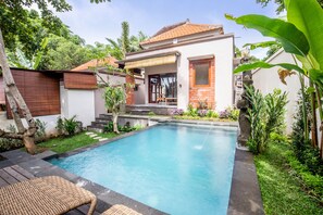 A swimming pool with a wooden deck and a small outdoor seating area. - Sari Bamboo Villas (Ubud)