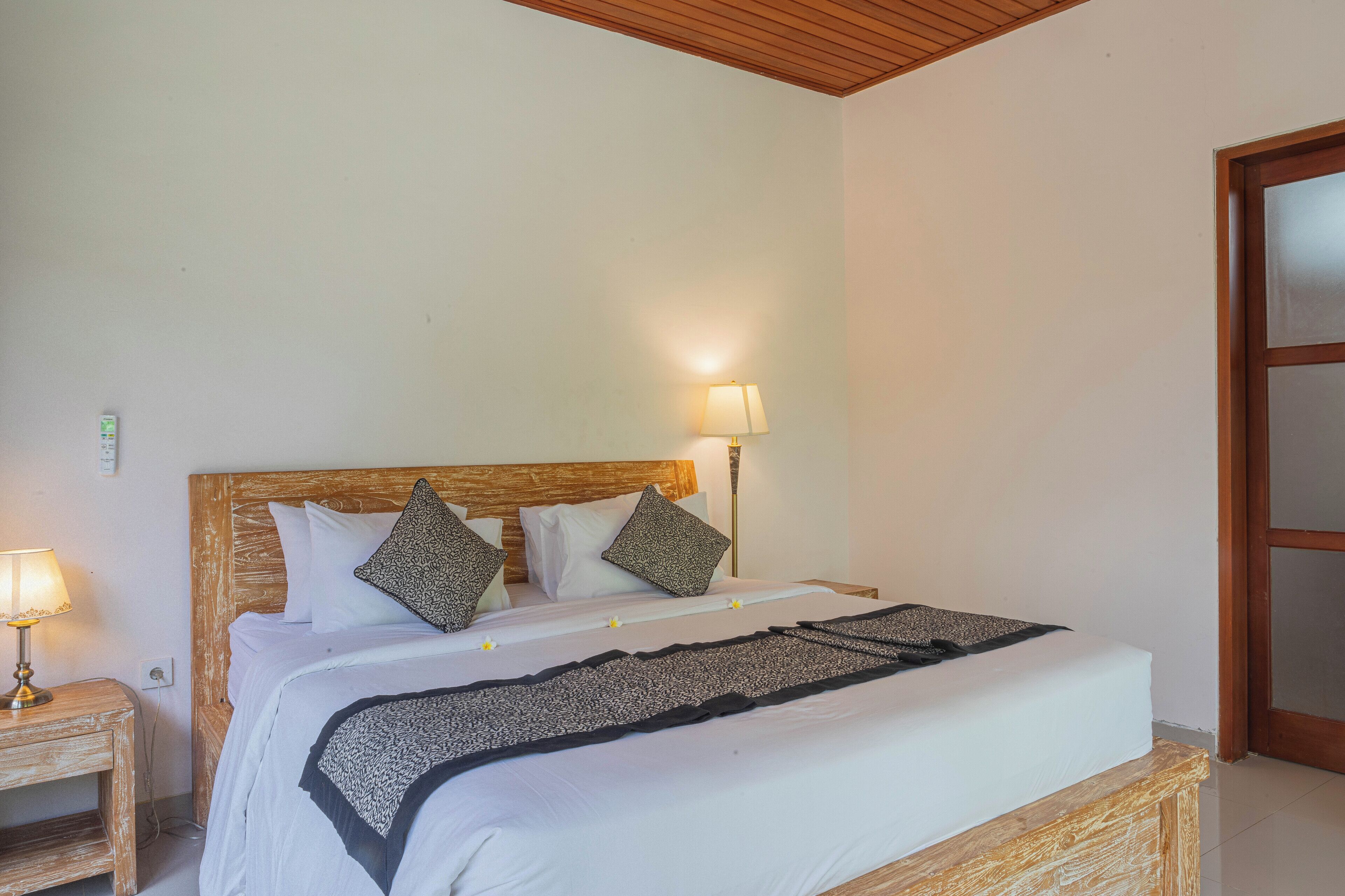 A neatly made bed with a wooden headboard, two bedside lamps, and a white wall.