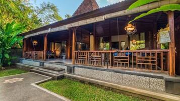 A wooden structure with a tiled roof, a covered porch with seating, and a stone pathway leading to the entrance.