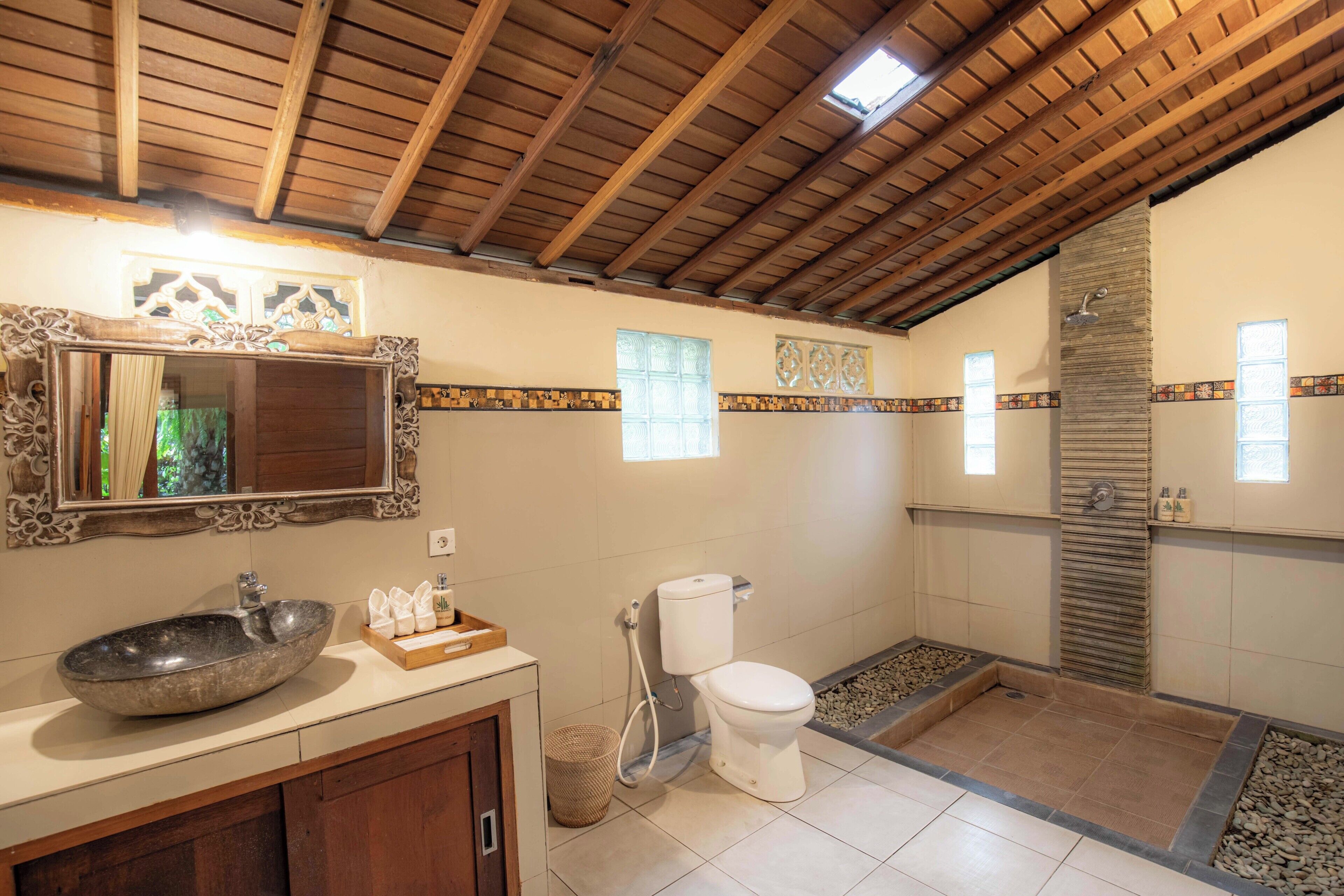 Une salle de bain avec un lavabo en pierre, des toilettes, une douche et un miroir orné d’un cadre travaillé.