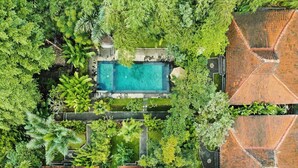 An aerial view of a residential area with a swimming pool surrounded by lush greenery and multiple houses with tiled roofs. - Sari Bamboo Villas (Ubud)