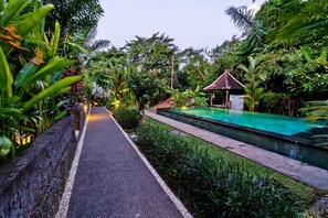 A pathway leading to a pool surrounded by lush greenery and a small gazebo. - Sari Bamboo Villas (Ubud)