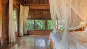A wooden room with a bed under a canopy, large windows, and curtains. - Sari Bamboo Villas (Ubud)