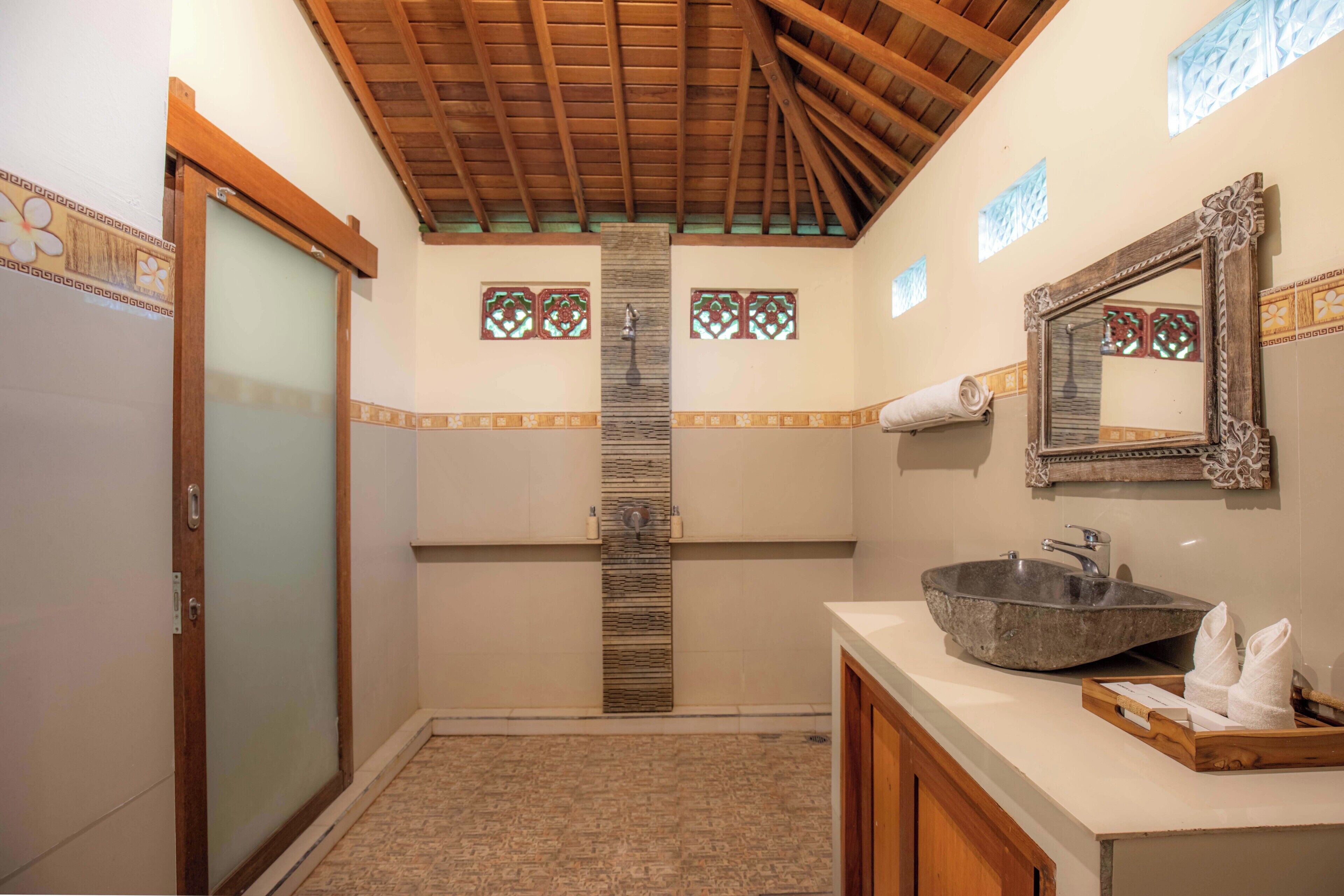 Un baño con techo de madera, un pilar de piedra, un lavamanos grande y un espejo con marco decorativo.