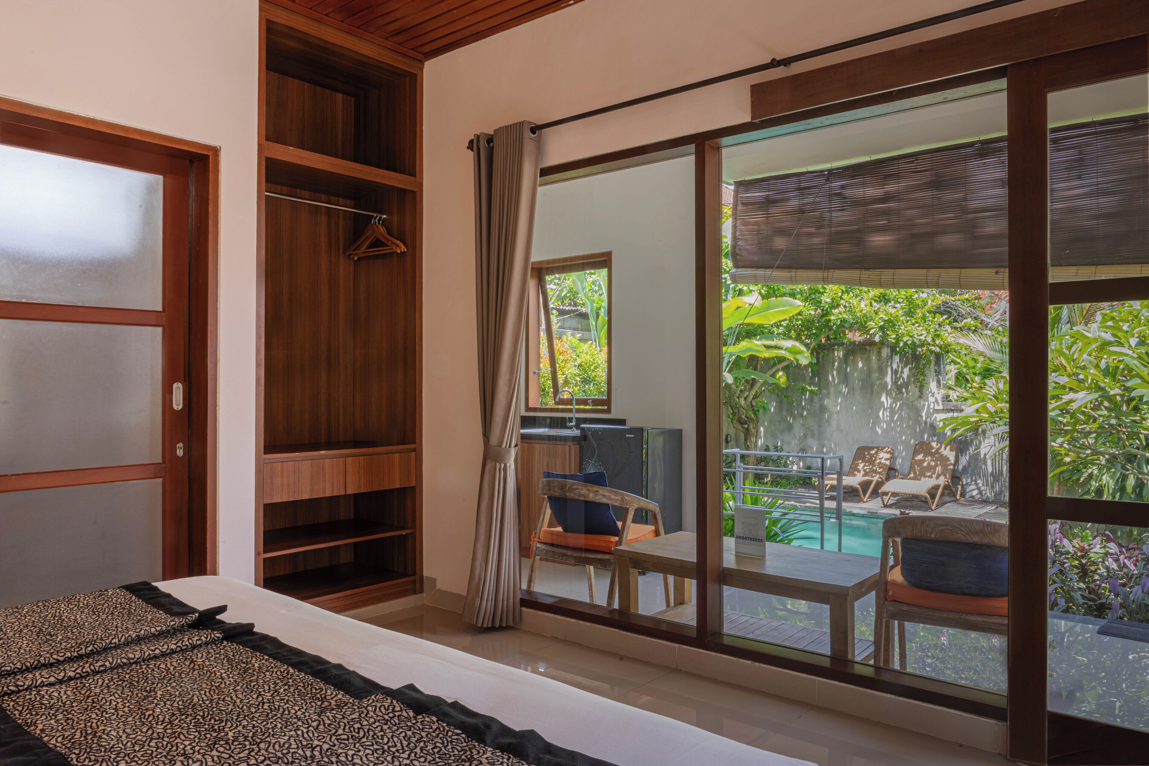 A bedroom with a large sliding glass door leading to a balcony with a pool and lush greenery.