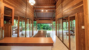 A spacious wooden interior with a long table, large windows, and a view of the outdoors. - Sari Bamboo Villas (Ubud)