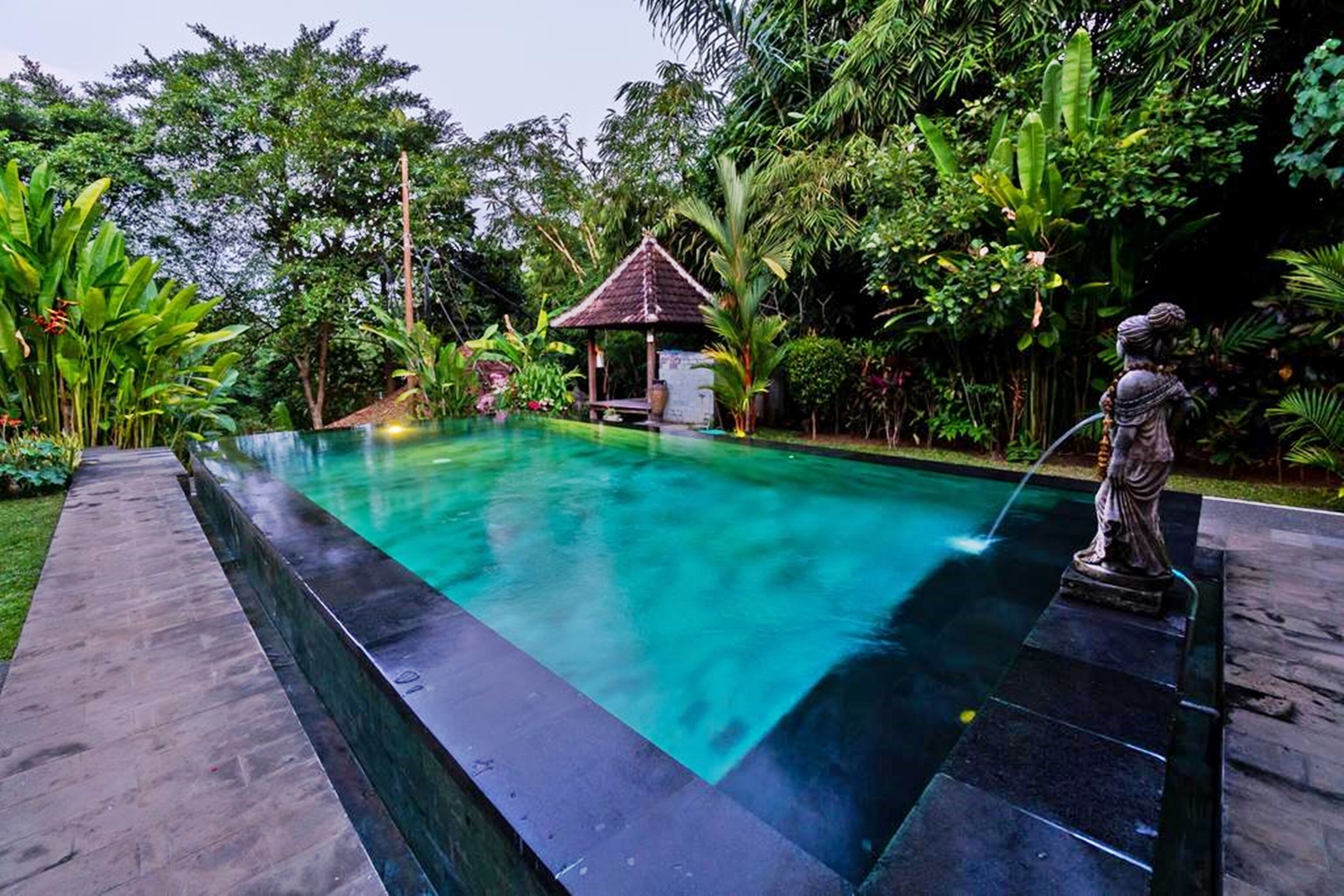 A rectangular pool with a tiled edge, surrounded by lush greenery and a gazebo.