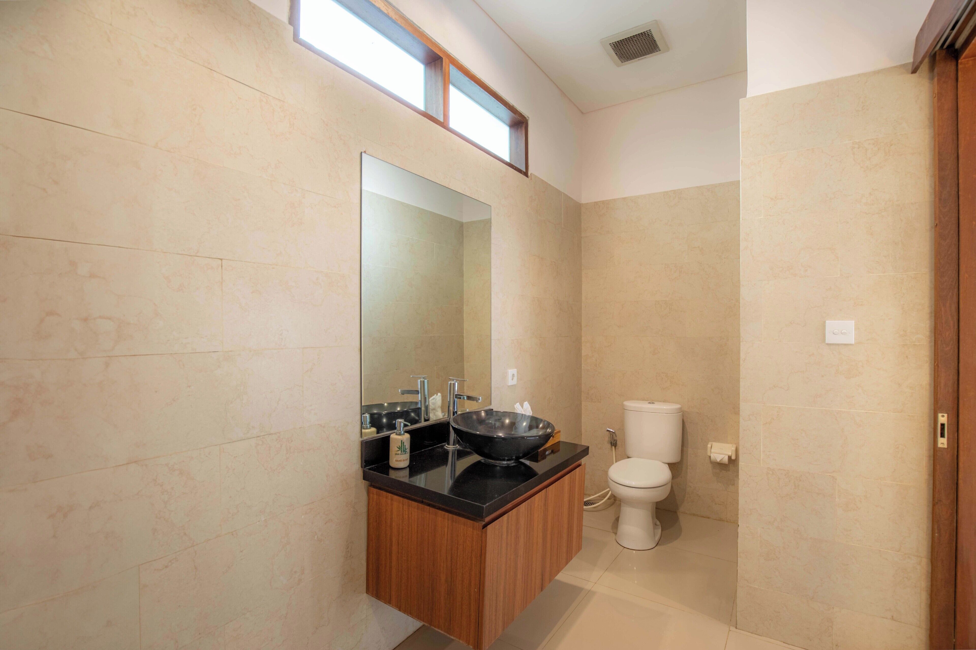 A bathroom with a black sink, wooden vanity, and a toilet.