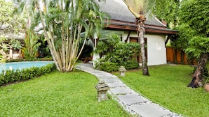 Un jardín tropical con piscina, un sendero de piedra y un edificio tradicional con techo de tejas.