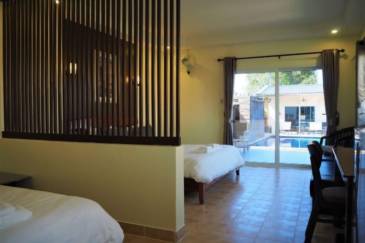A hotel room with two beds, a dining area, and a view of a pool and building.