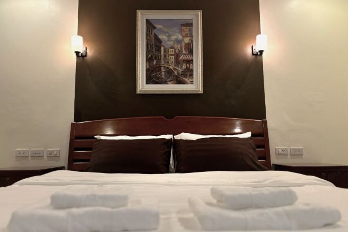 Una habitación de hotel con una cama, dos lámparas fijadas a la pared y un cuadro enmarcado sobre la cama.