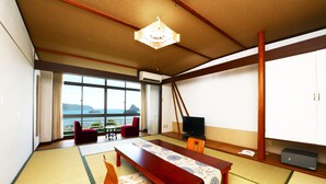 Ein traditioneller japanischer Raum mit Tatami-Böden, einem niedrigen Holztisch, einem Fernseher und Meerblick.