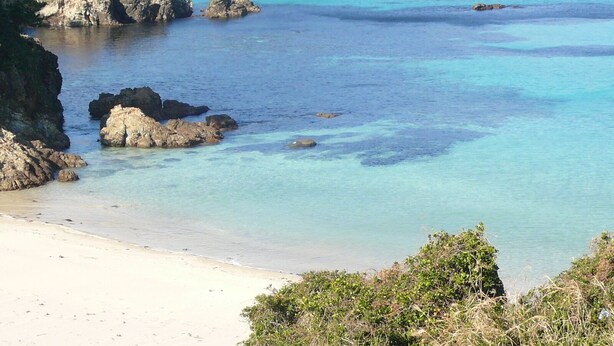 Eine Küstenlandschaft mit klarem türkisblauem Wasser, Felsformationen und einem Sandstrand.