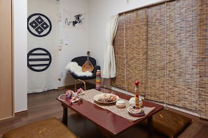 Traditional Japanese-style room with tatami flooring and a low table, featuring a black chair and bamboo blind.