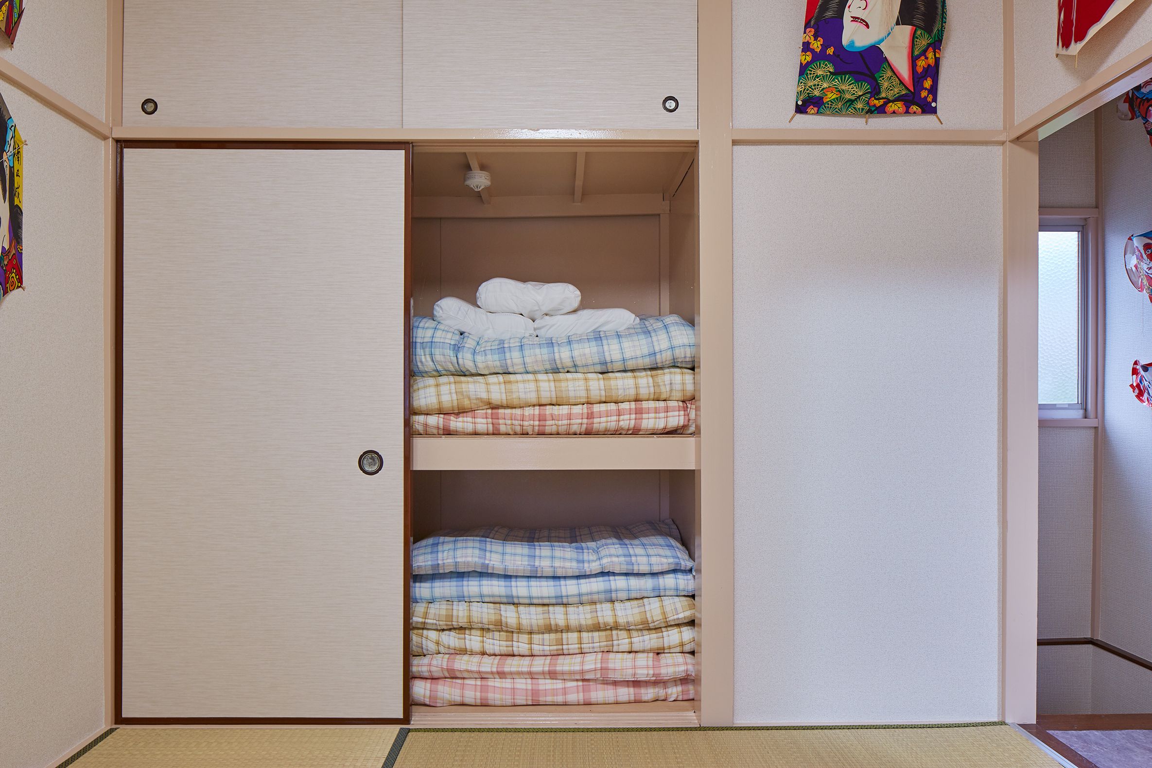 A room with a wardrobe containing folded bedding and a decorative item on the top shelf.