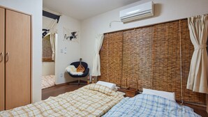 Een slaapkamer met twee bedden, een stoel, een gitaar en een raam met bamboeblamen.
