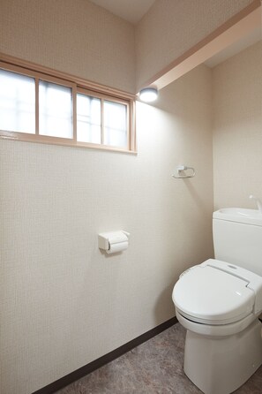A bathroom with a toilet, a paper towel dispenser, and a window with blinds.