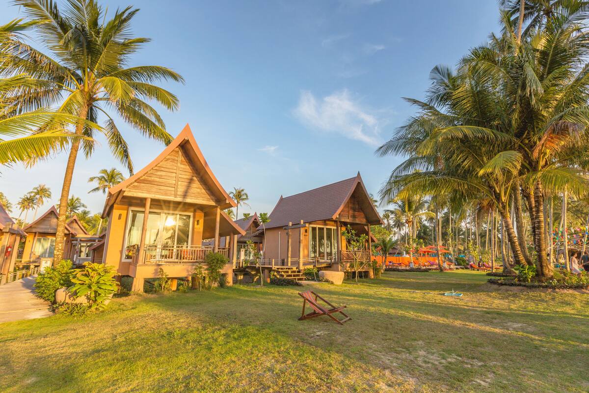 Een resort met houten bungalows, een gazon en palmbomen.
