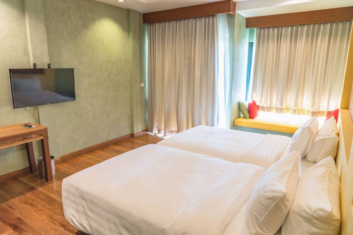 Een hotelkamer met twee bedden, een televisie en gordijnen.