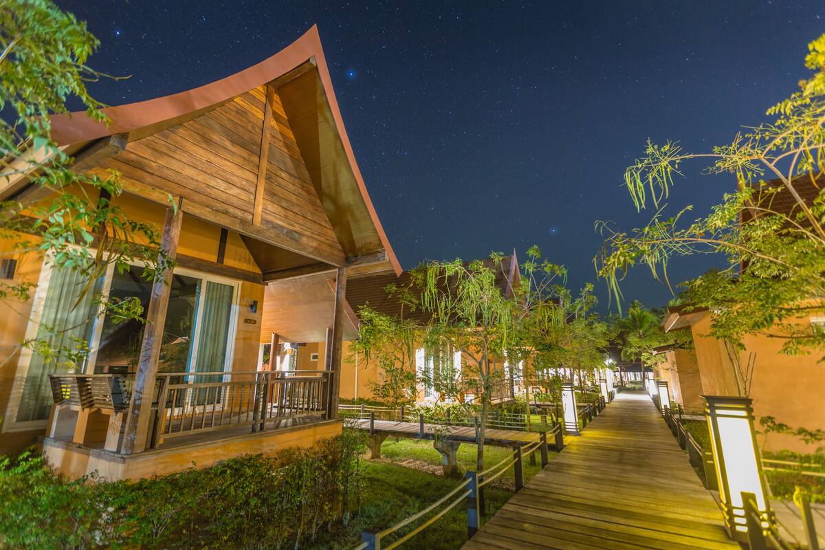 ’s Nachts uitzicht op een resort met een houten gebouw, een overdekte doorgang en weelderige begroeiing.
