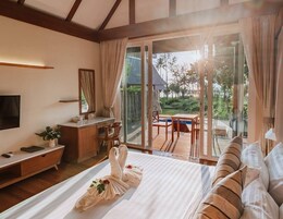 Habitación de hotel con cama, mesita de noche y escritorio con silla. Amplia ventana con cortinas y vistas al exterior.