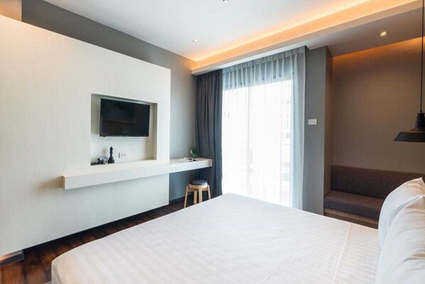 Quarto de hotel moderno com uma cama grande, uma TV montada na parede, um banquinho pequeno e um banco.