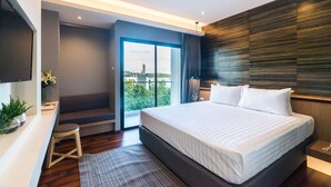 A modern hotel room with a large bed, a desk, and a view of the city through a sliding door. - Sea Me Spring Tree Hotel - Adults only (Pattaya)