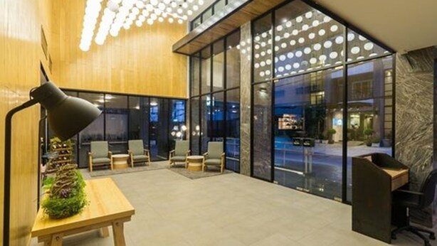 A modern lobby with a wooden reception desk, a black floor lamp, and a seating area with chairs. - Sea Me Spring Tree Hotel - Adults only (Pattaya)