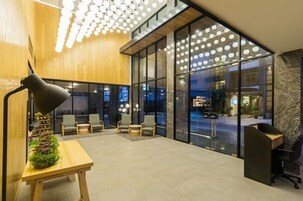 Un vestíbulo moderno con un mostrador de recepción de madera, una lámpara de pie negra y una zona de estar con sillas.