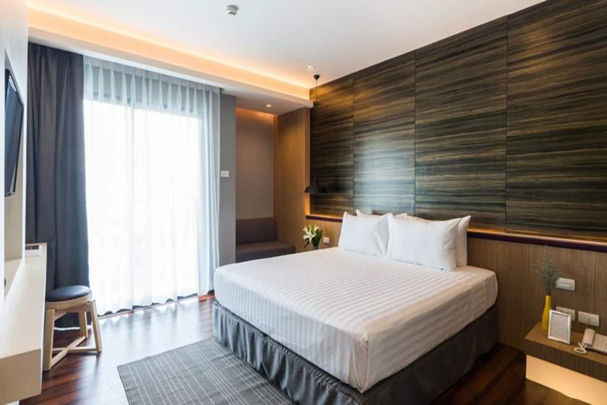 A modern hotel room with a large bed, a desk, and a view of the outdoors.