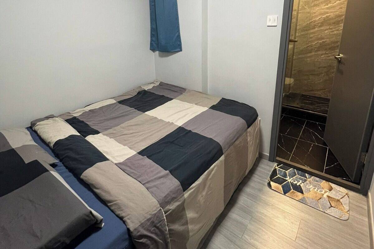 Ein kleines Zimmer mit einem Einzelbett, einer karierten Bettdecke, einem blauen Vorhang und einer Tür zu einem Badezimmer mit gefliestem Boden.