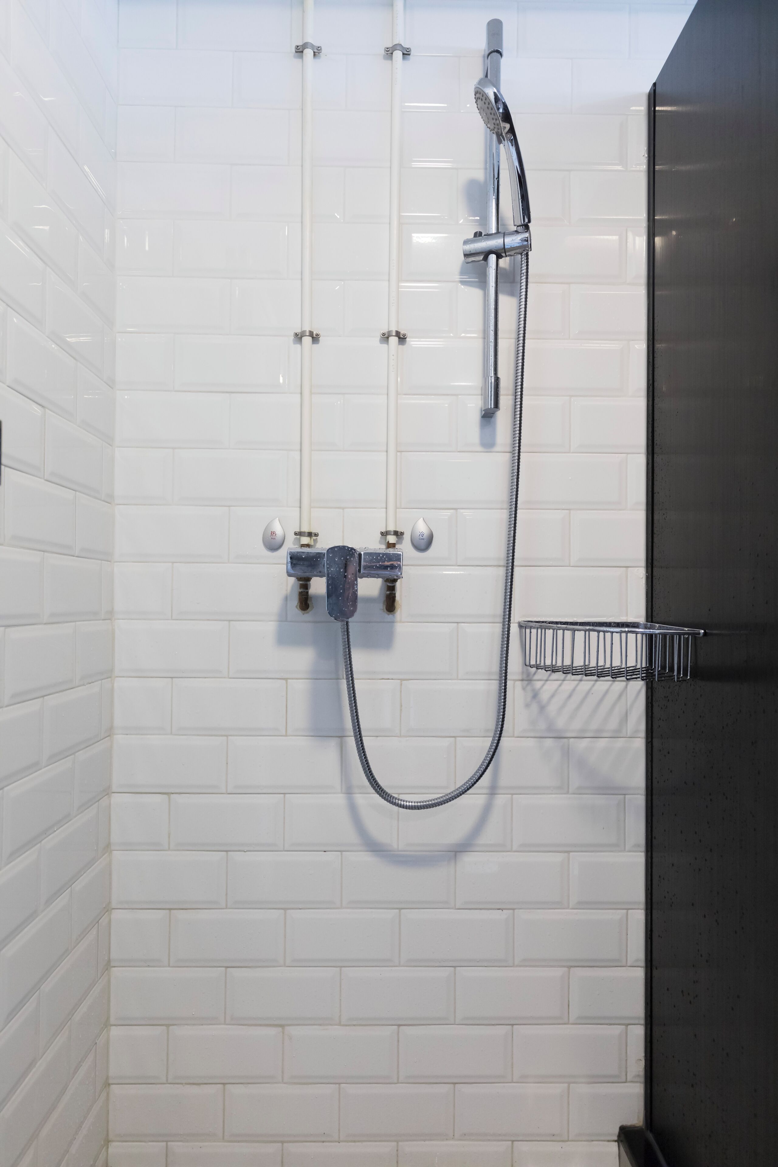 A bathroom with white tiled walls, a shower with a handheld showerhead, and a metal towel rack.