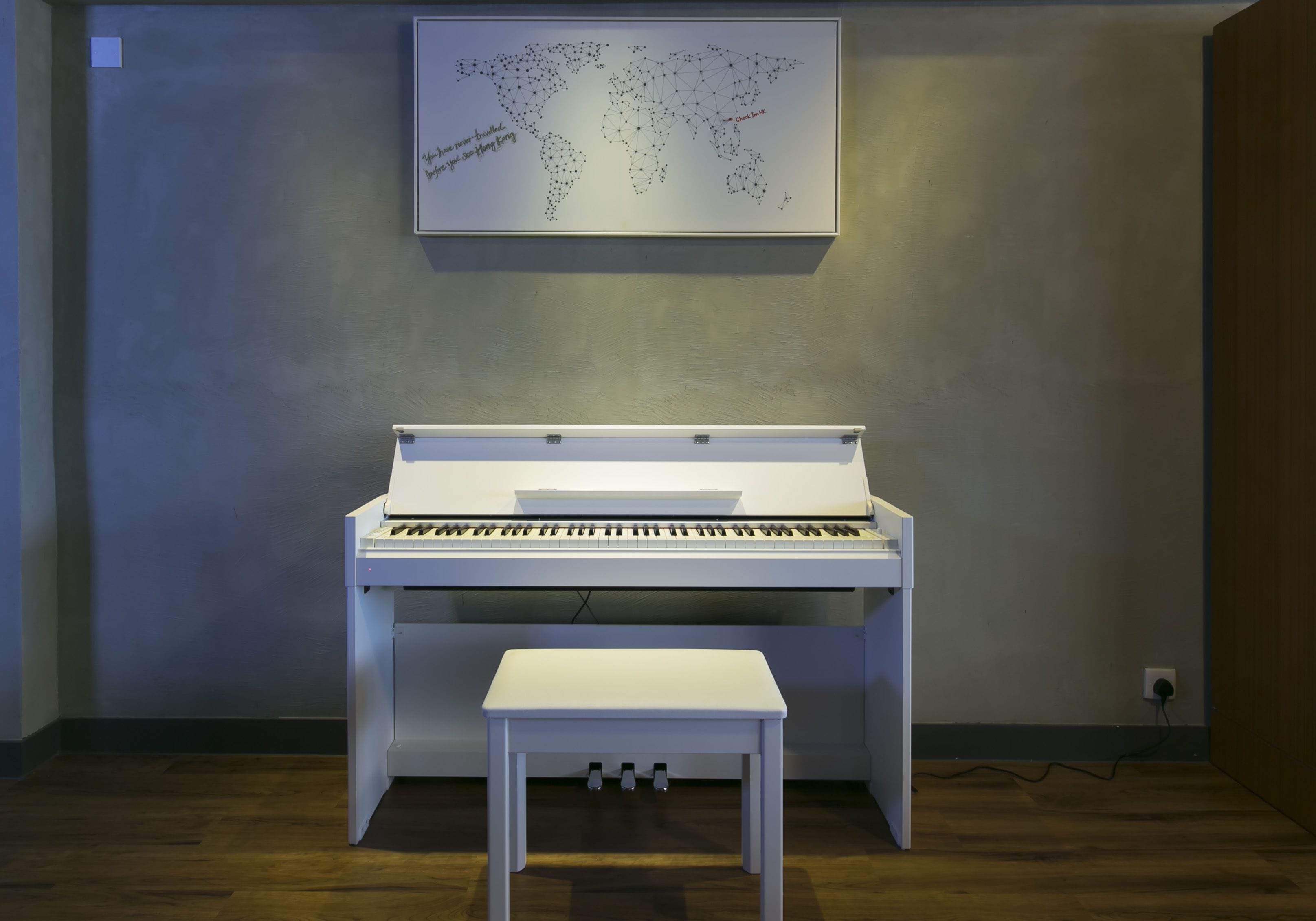 A piano with a bench in front of it, a world map on the wall, and a power outlet on the right.