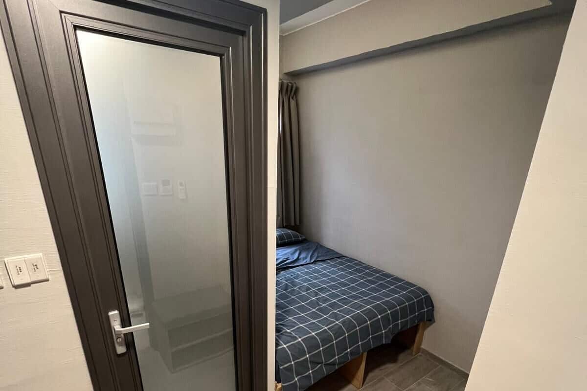 Ein kleiner, kompakter Raum mit einem Bett, einer Tür und einer Bank.