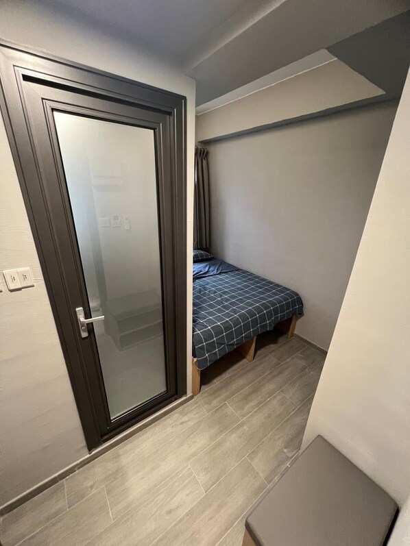 Une petite pièce, de taille modeste, comprenant un lit, une porte et un banc.