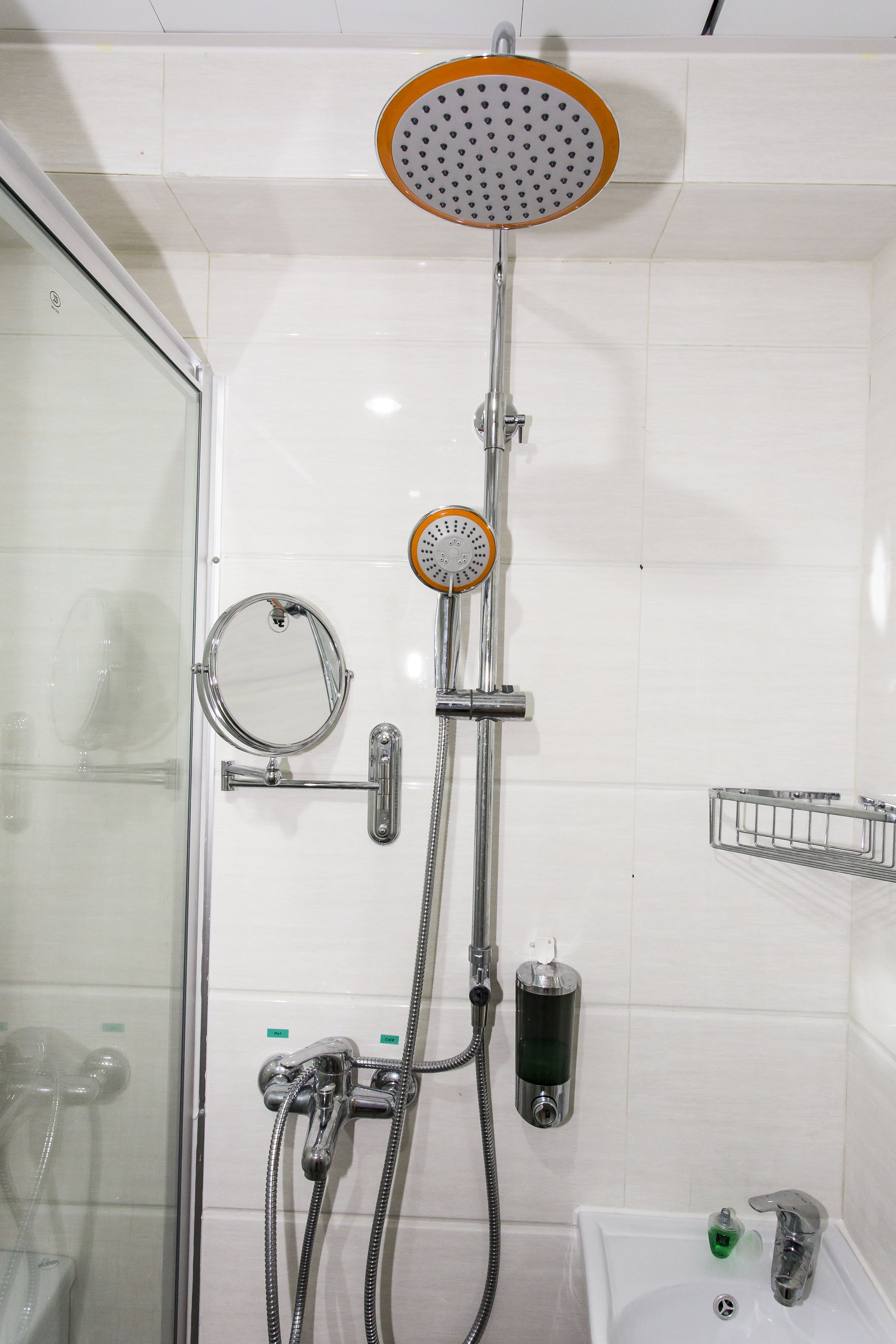 A bathroom with a glass shower enclosure, a handheld showerhead, a wall-mounted faucet, a soap dispenser, and a small sink with a mirror.