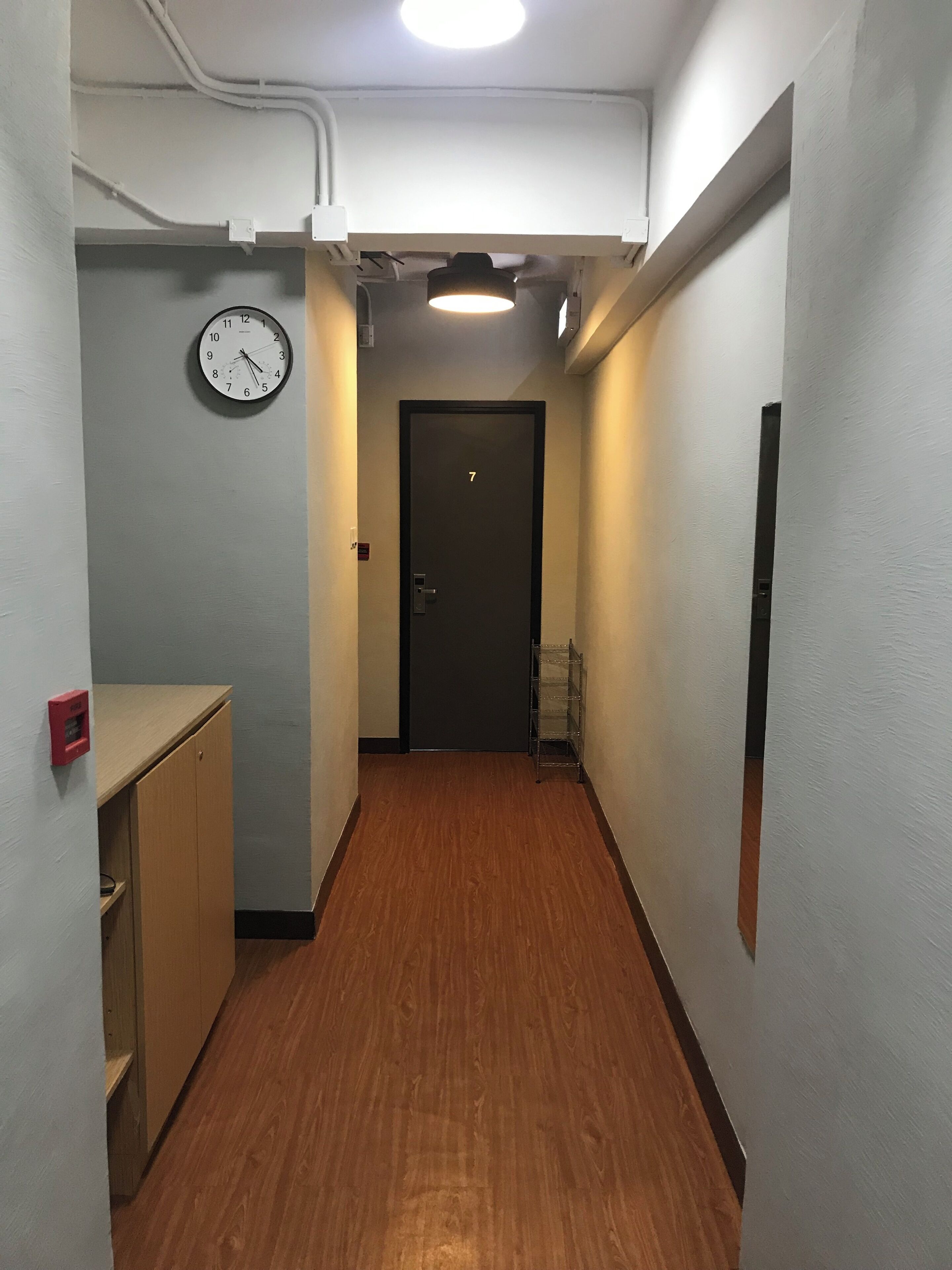 Un couloir étroit avec un plancher en bois, une horloge sur le côté gauche et une porte portant le numéro 7 au bout.