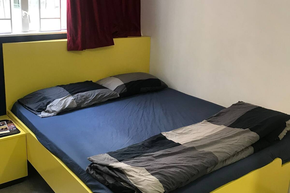 Ein Bett mit gelbem Gestell, blauer Bettwäsche und einem roten Vorhang.