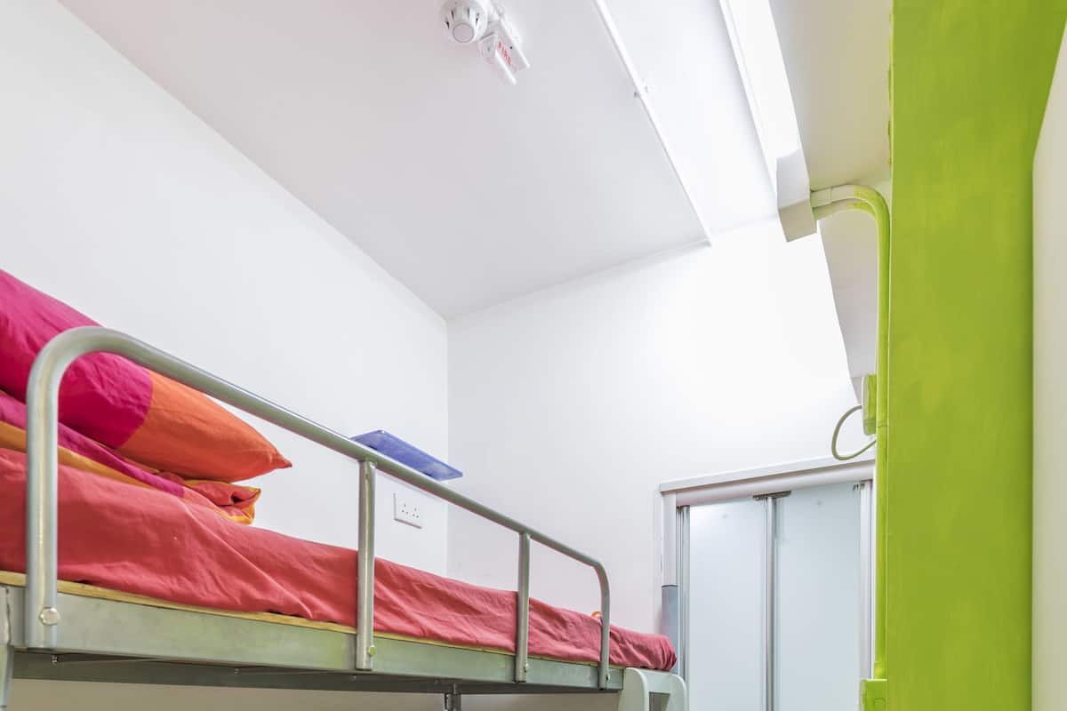 Ein Schlafraum mit Etagenbetten, einer grünen Tür, einer weißen Decke und einem kleinen Regal.