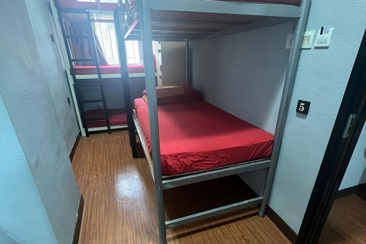 Ein Schlafsaalzimmer mit Etagenbetten, Holzboden und einem Fenster mit Vorhängen.