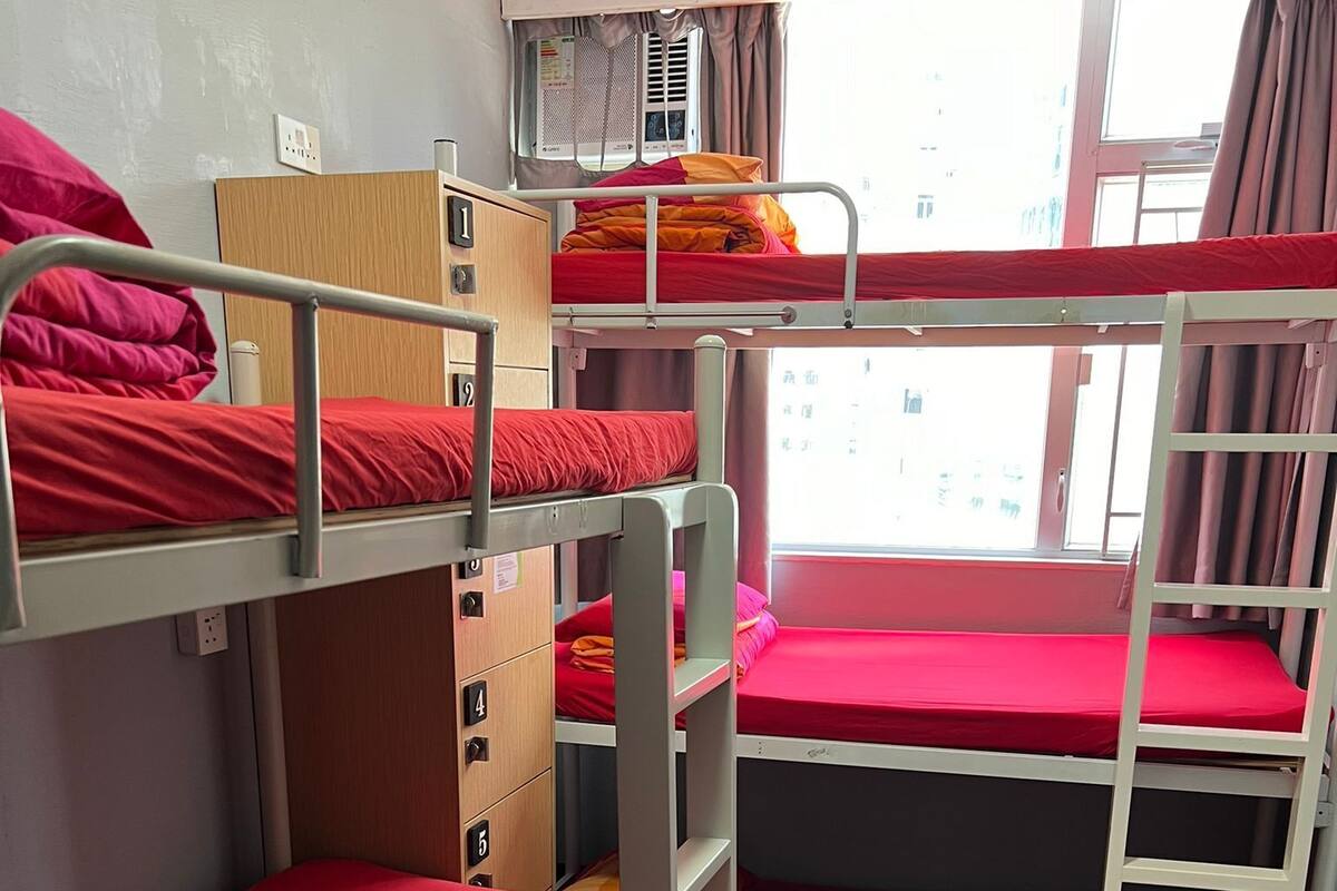 Ein Schlafsaalzimmer mit Etagenbetten, Holzboden und einem Fenster mit Vorhängen.