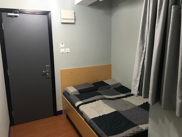 Une petite chambre avec un lit simple, une tête de lit en bois, une porte sombre et un mur de couleur claire.