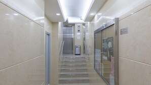 Et moderne elevatormiljø med glasdør, metalelevator og trappe med tæppe.