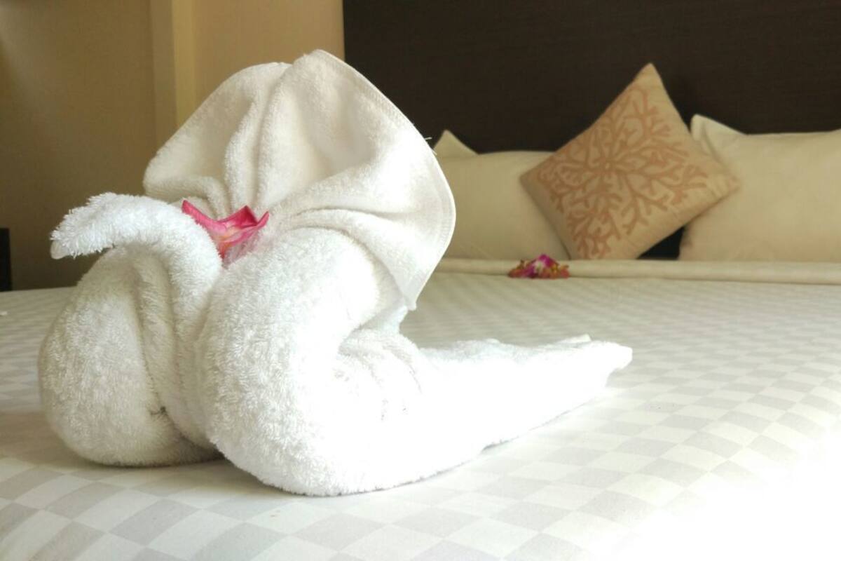 A neatly made bed with a white blanket and a swan-shaped towel.