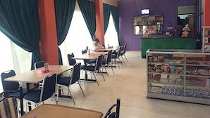 A restaurant with multiple tables and chairs, a counter with a display case, and a ceiling fan. - Hotel Fiducia Kaji (Jakarta)